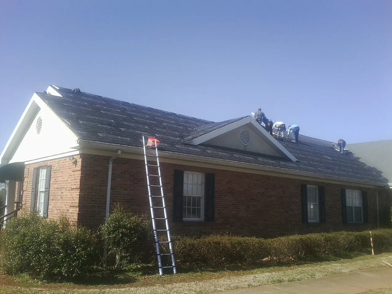 Crew tearing shingles off a brick ranch roof with a ladder set — Emergency Roof Repair work by our crew in Hebron
